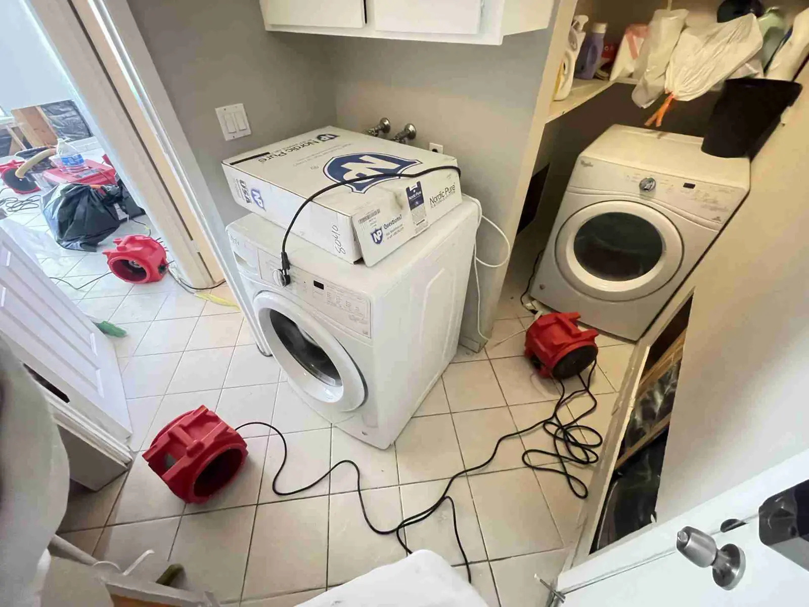 Air movers drying a laundry room with the washer and dryer pulled out