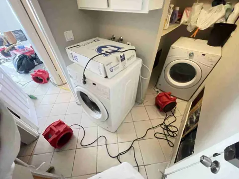 Air movers drying a laundry room with the washer and dryer pulled out