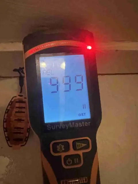 Moisture meter reading a saturated baseboard
