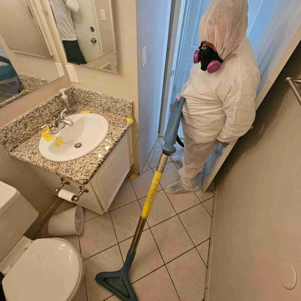 Technician in a respirator and protective suit extracting water from a bathroom